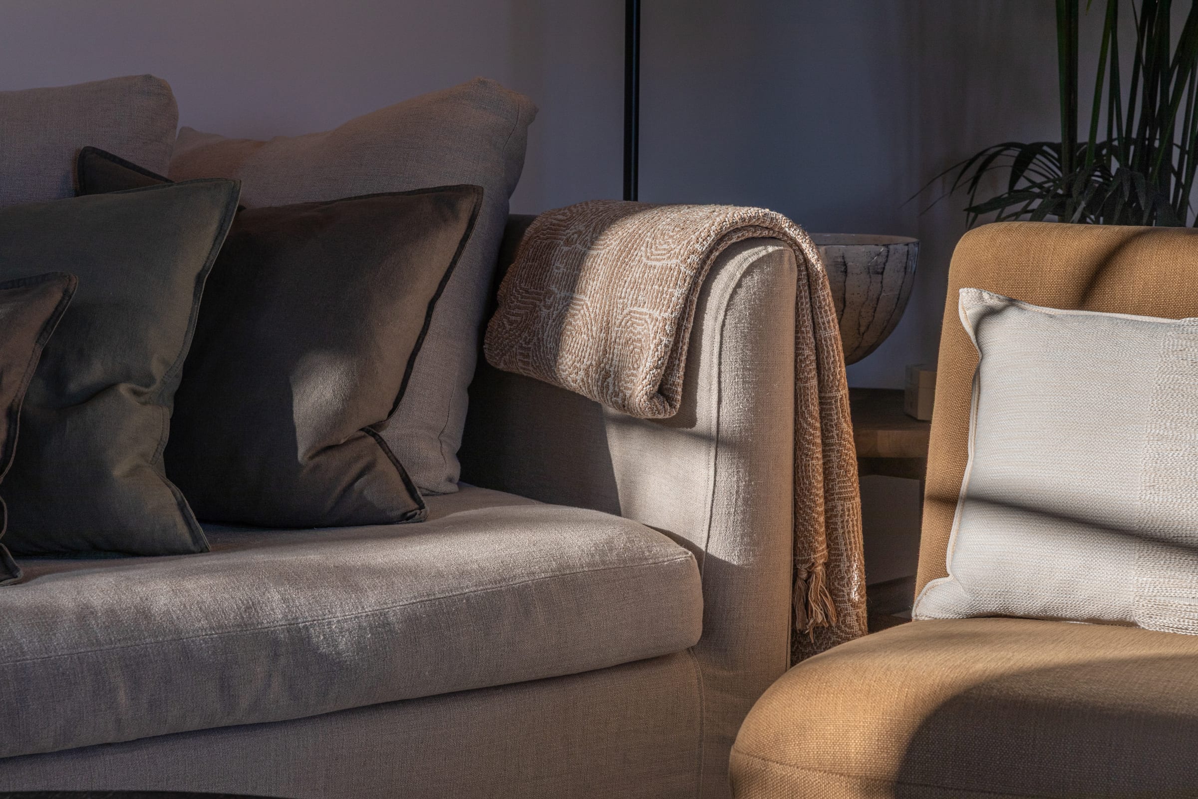 Layered cushions and a woven throw on linen sofas in a softly lit living room, styled by Seijaku Studio