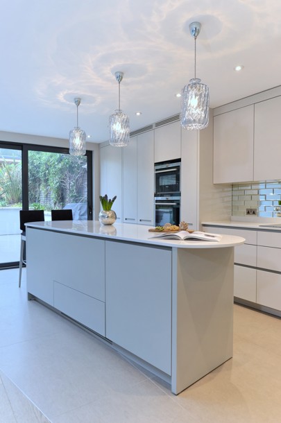 Curved white kitchen island with glass pendant lights, open to the dining table beyond