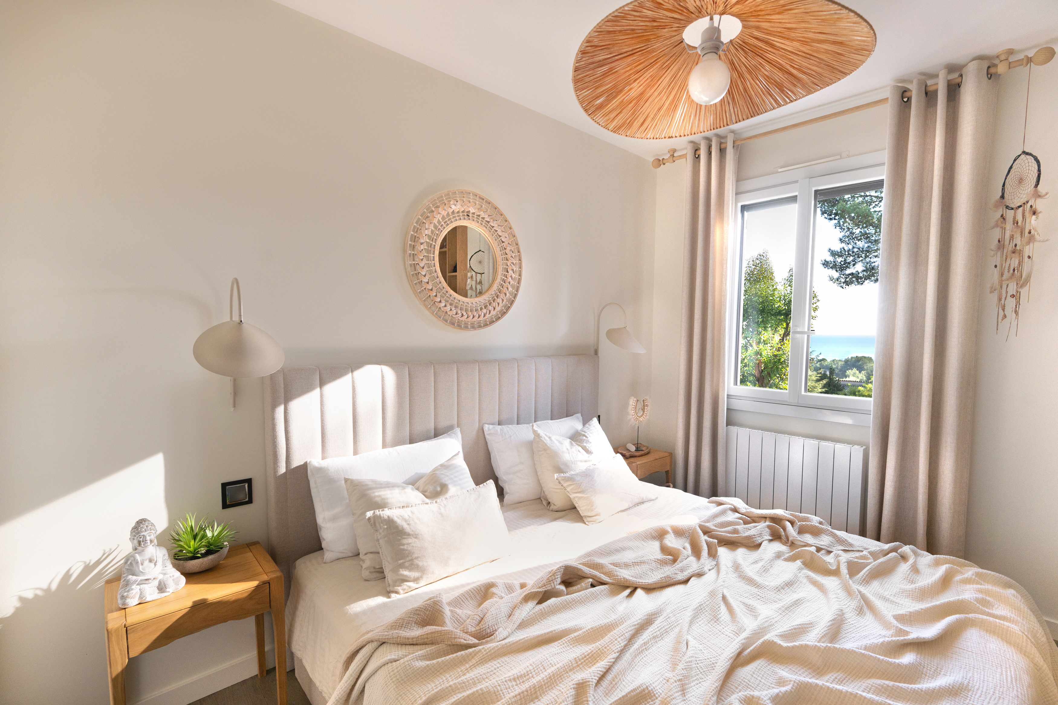 Bedroom with a channelled headboard, round woven mirror, and a rattan pendant light above the bed