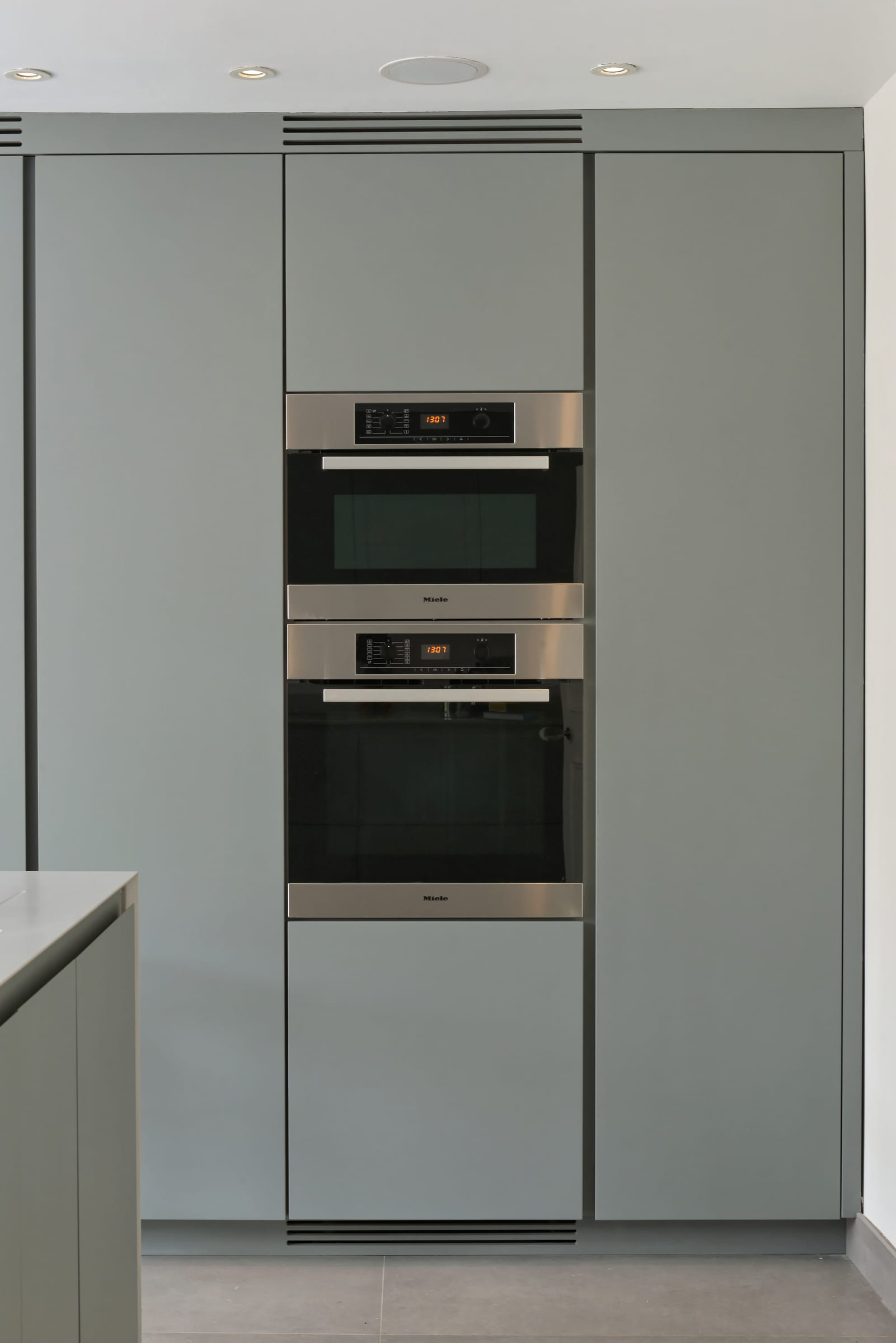 Grey spray-lacquered pantry cabinetry with a stacked Miele oven and microwave