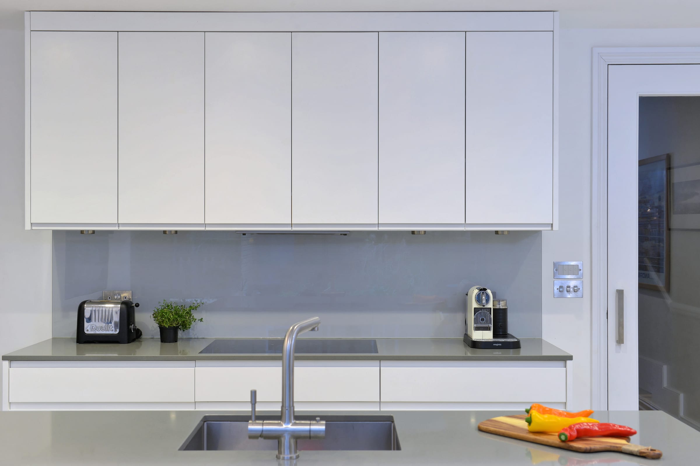 White kitchen with a pale grey glass splashback, toaster, and coffee machine