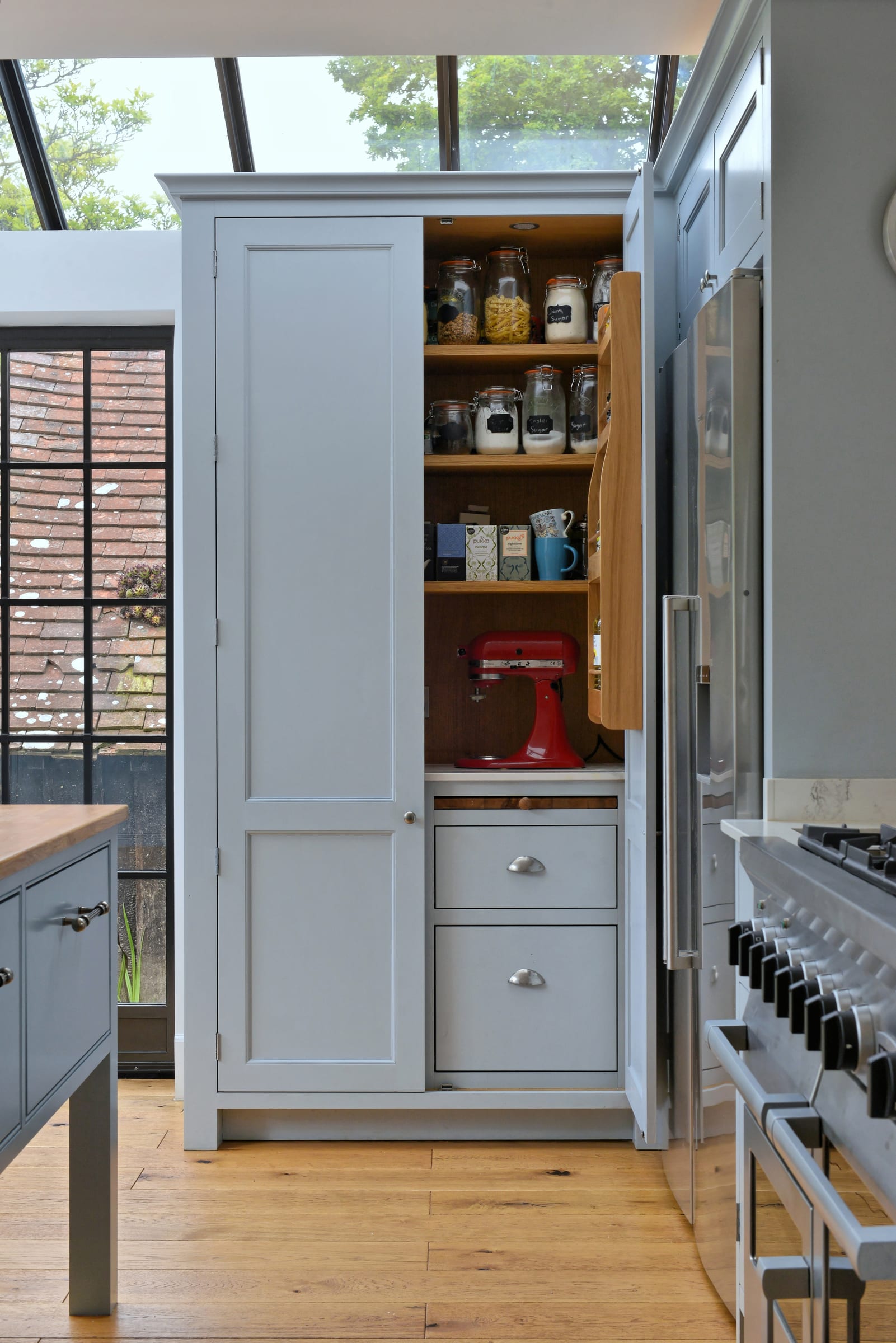 Open bespoke pantry with in-frame cabinetry, glass storage jars, and a red stand mixer in a Weybridge shaker kitchen