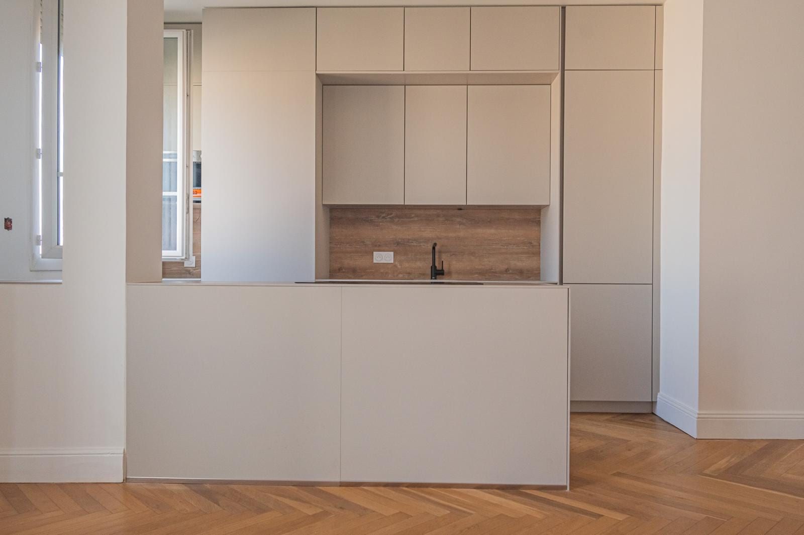 Sleek white kitchen with a wood-panelled backsplash and herringbone parquet flooring