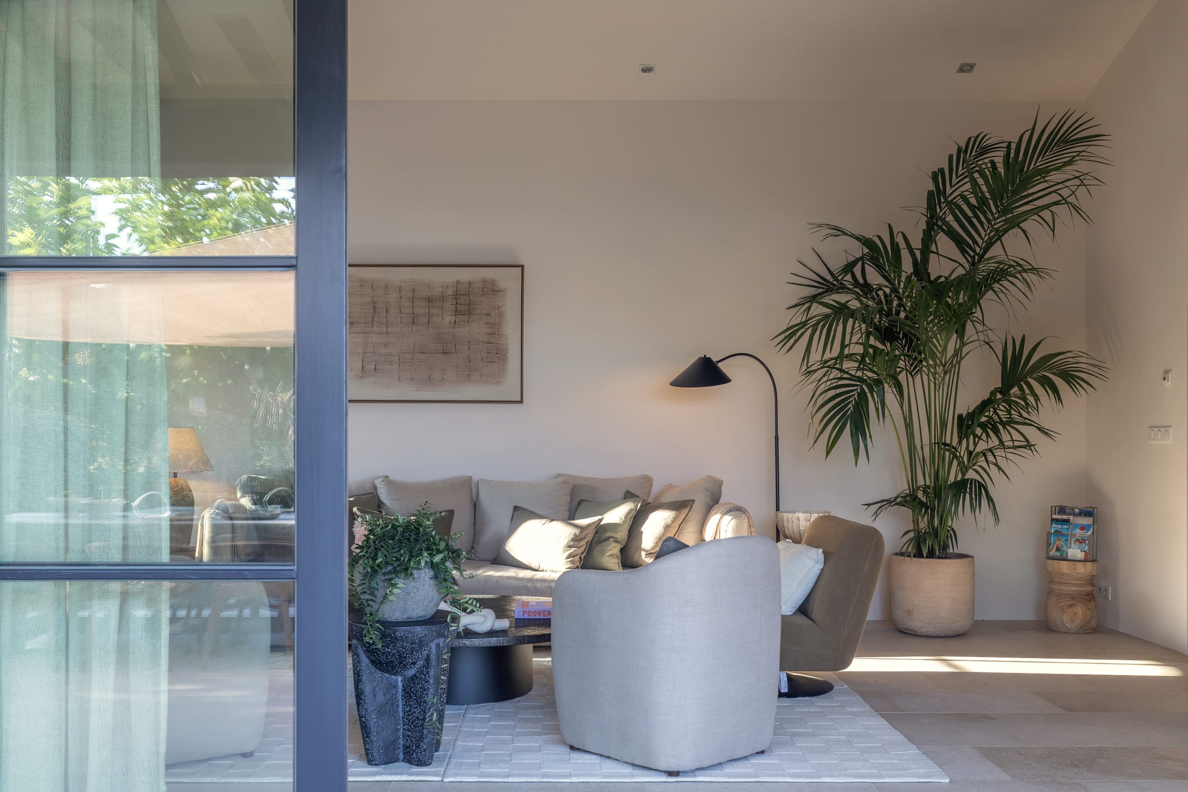 Living room corner with framed artwork, a black floor lamp, and a large potted palm by the glass doors