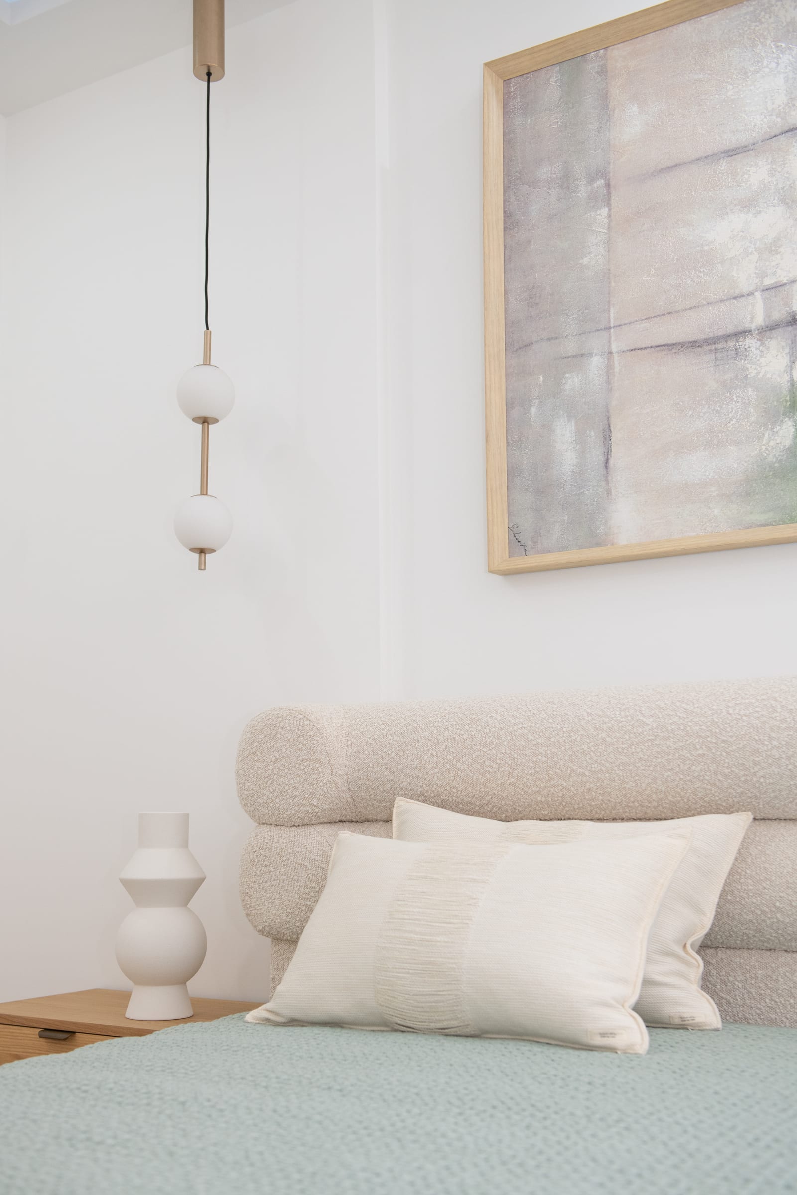 Sage and warm-white bedroom in the Serenity apartment in Menton, with a boucle headboard, ceramic lamp, and brass pendant light