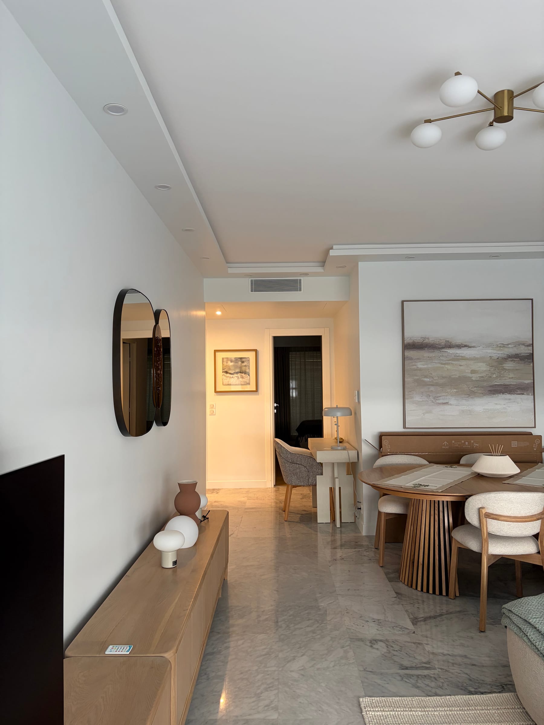 Dining nook with a brass sputnik chandelier, framed art, and woven-back chairs on marble flooring